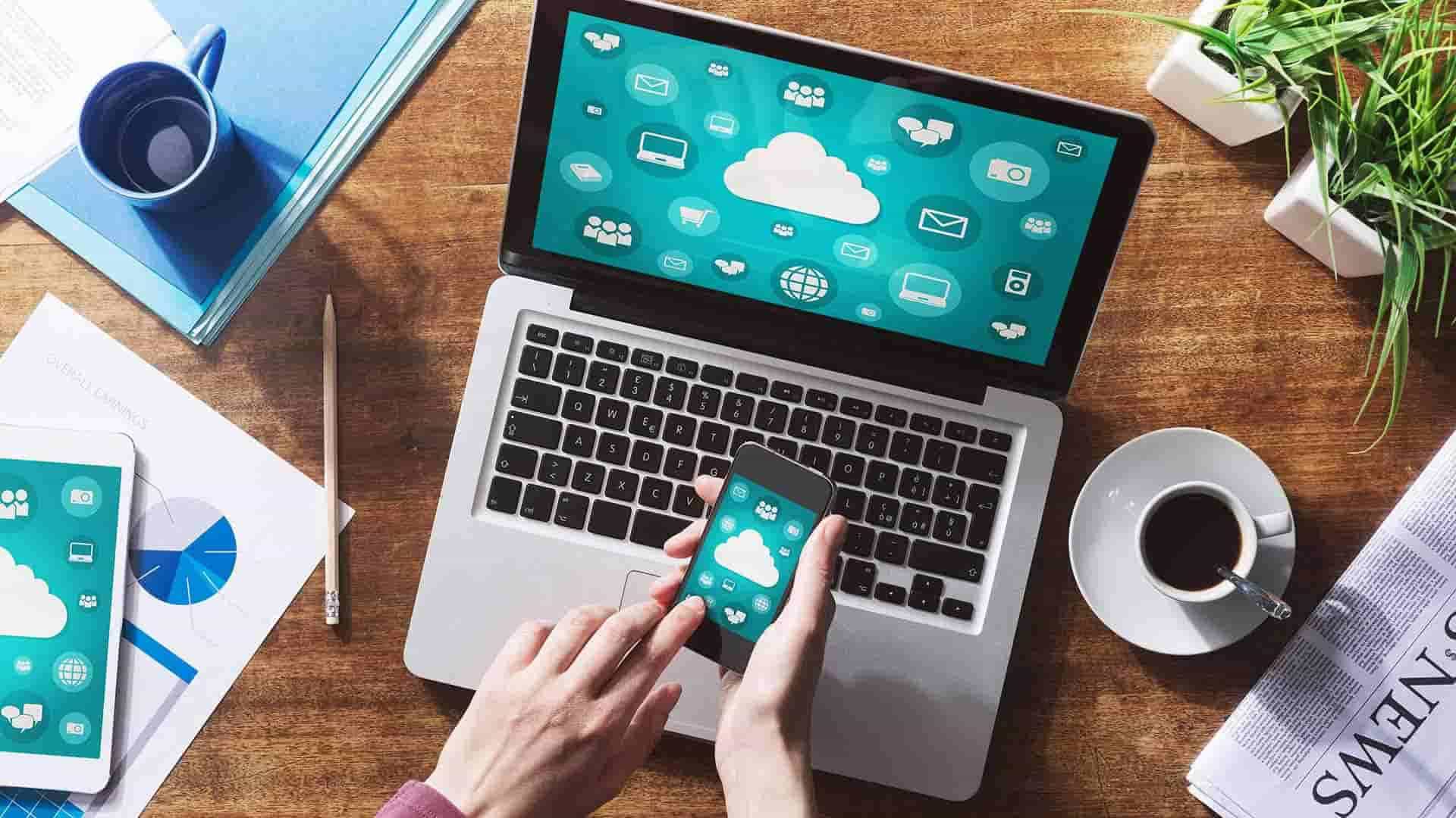 Laptop and smartphone on a desk displaying cloud and social media icons