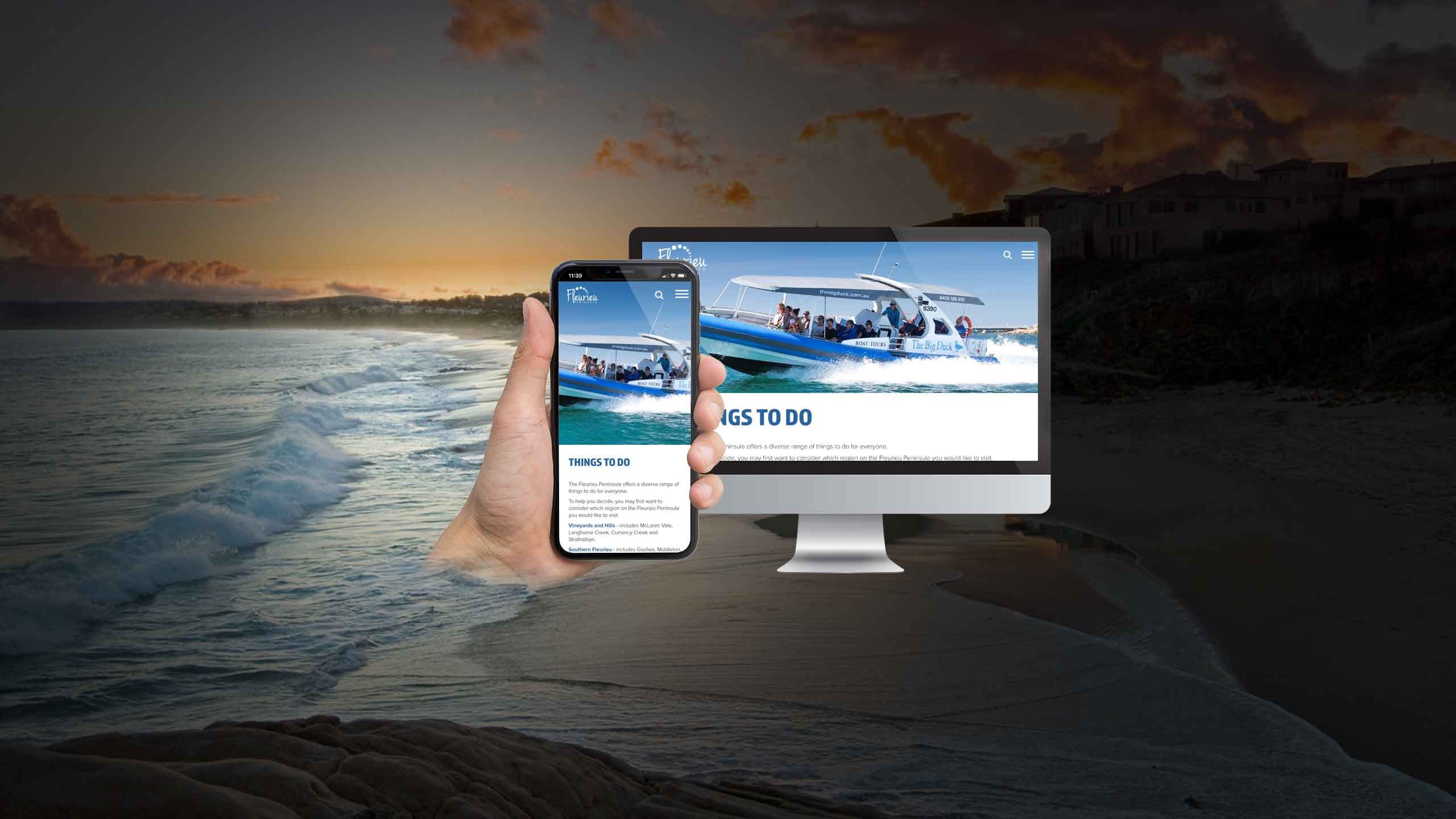 Fleurieu Peninsula Tourism website on a desktop monitor and smartphone, with a boat tour photo, over a beach at dusk