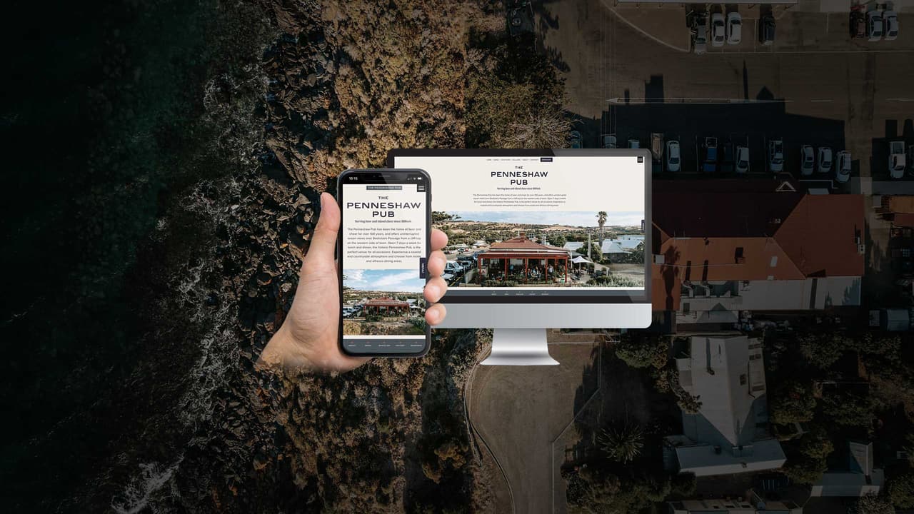 The Penneshaw Pub website homepage displayed on a desktop monitor and smartphone over an aerial coastal view
