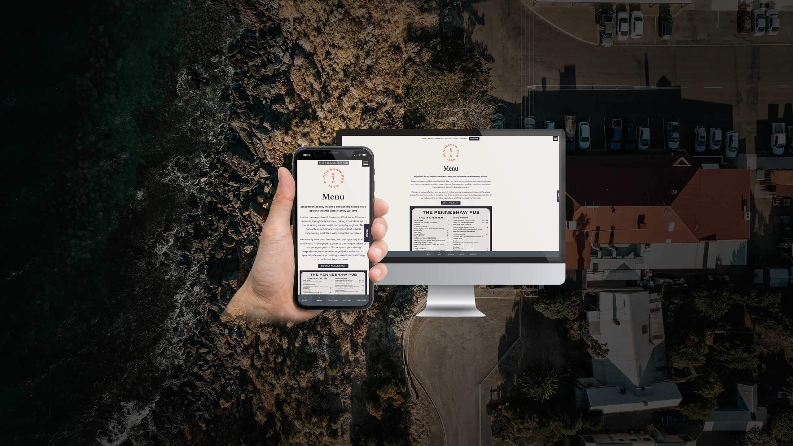 The Penneshaw Pub menu page displayed on a desktop monitor and smartphone over an aerial coastal view